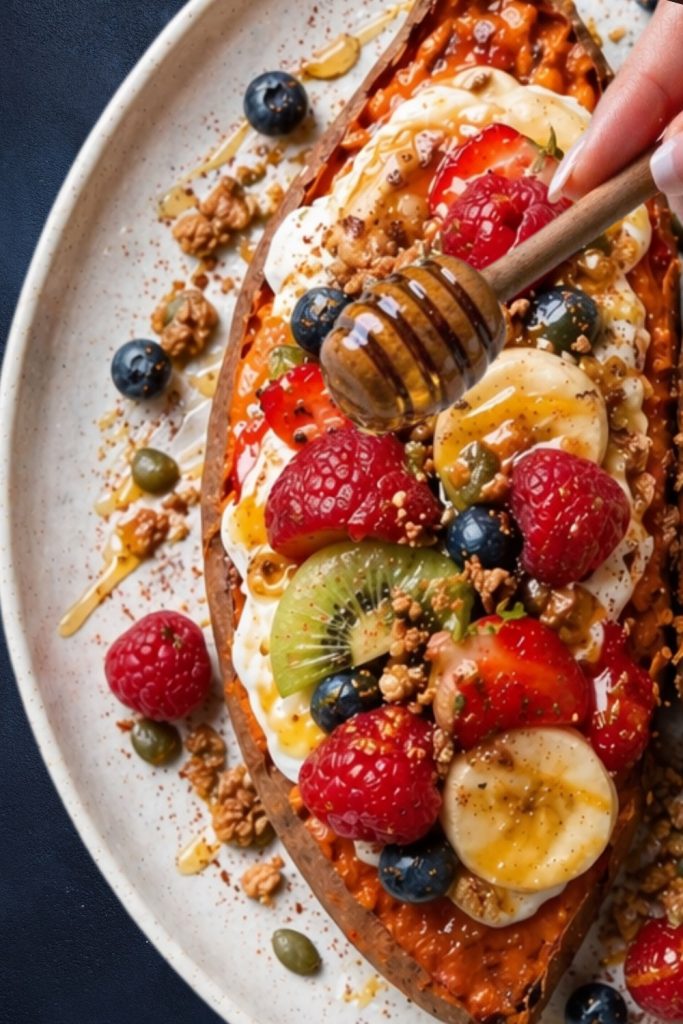 Berry vanilla sweet potato with yogurt, fresh fruits, granola and honey on a white plate.
