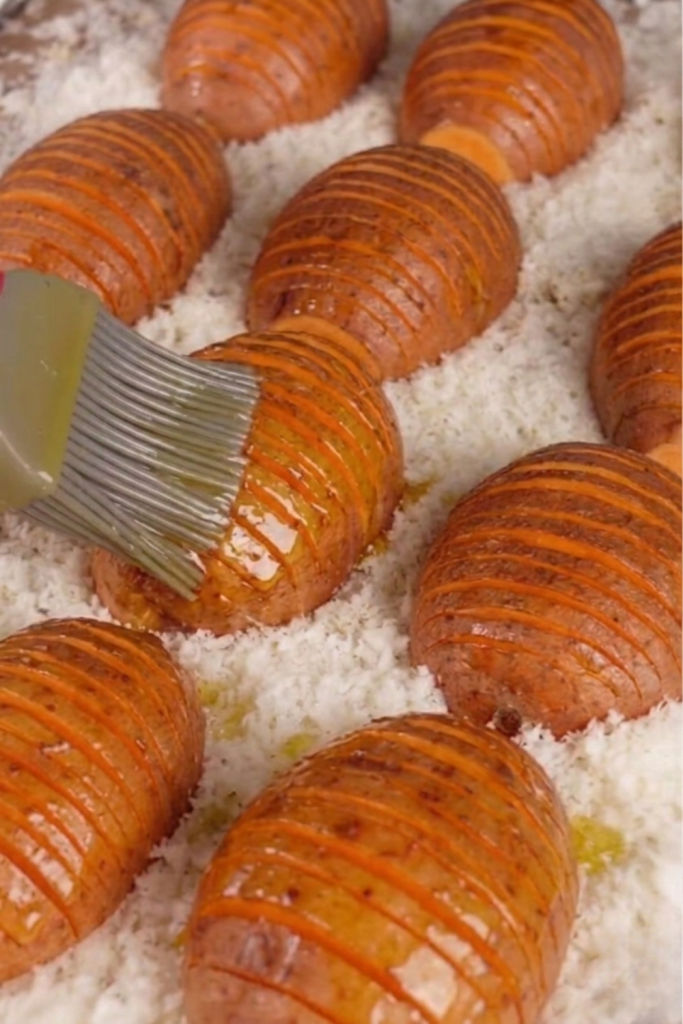 A top-down view of a baking tray filled with crispy, golden Garlic Parmesan Hasselback potatoes. The potatoes have thin, crunchy slices and are generously topped with melted parmesan cheese and fresh green herbs. Bright, aesthetic Mediterranean food photography.