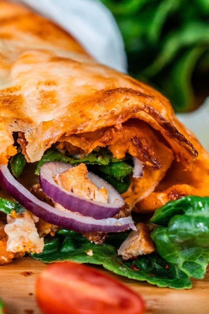Close-up of a sliced Italian melted sweet potato wrap with fresh spinach and red onions.