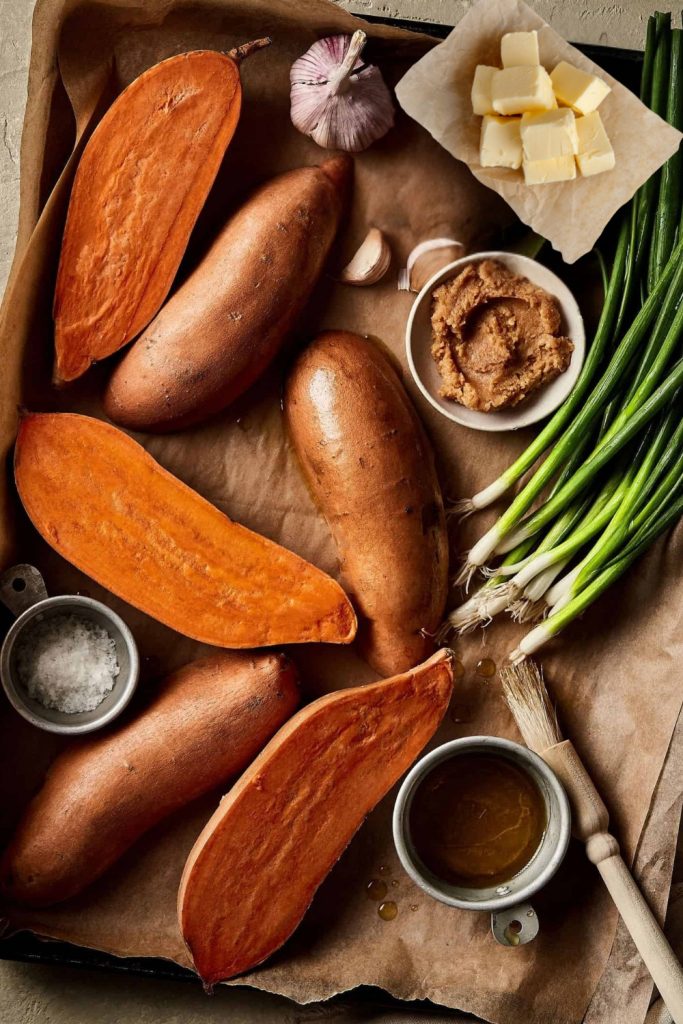 Raw sweet potatoes, miso paste, butter, and green onions on a rustic wooden background