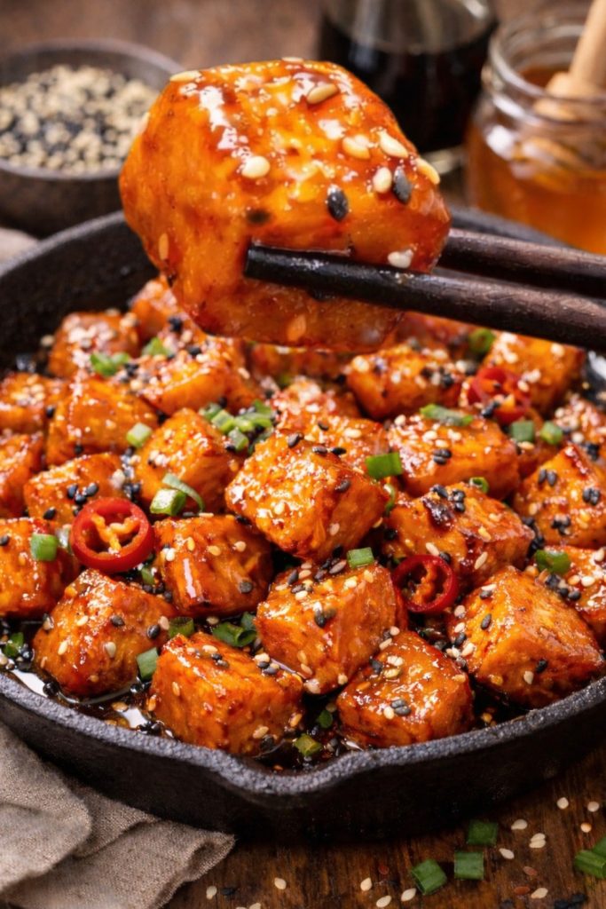 Sticky Asian-style sweet potato cubes in a cast iron skillet, topped with sesame seeds, spring onions and red chilli.