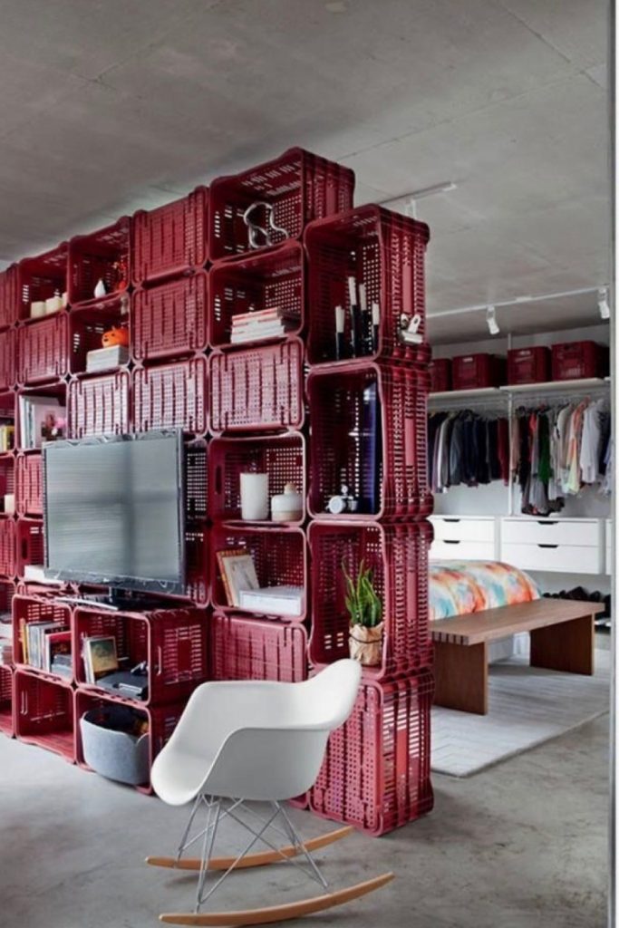 Creative wooden crate bookshelf used as a smart room divider in a small studio apartment to separate the living and sleeping areas.