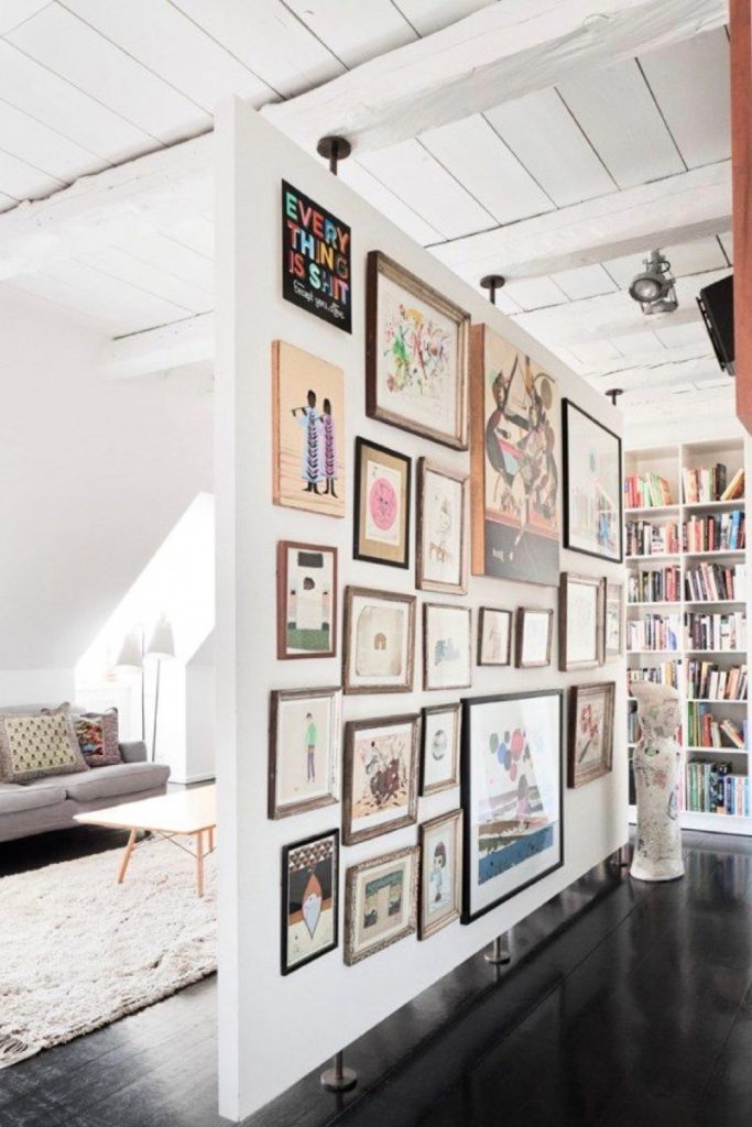 A free-standing gallery wall acting as a stylish room divider, featuring various framed art pieces and photographs in a modern loft.