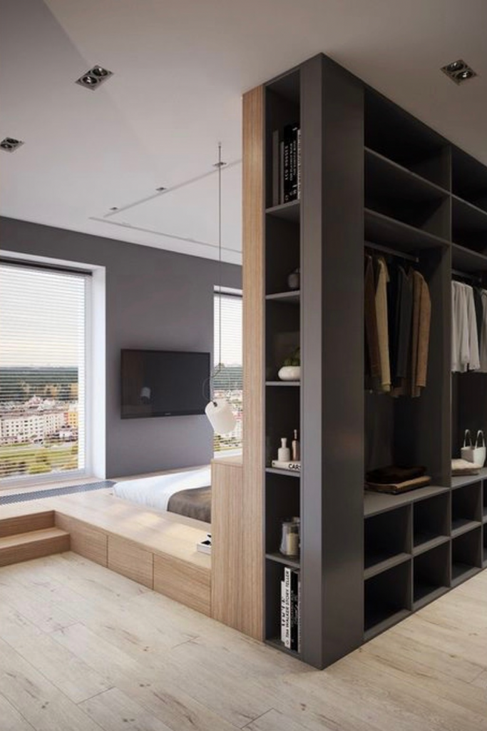 Custom floor-to-ceiling wardrobe used as a functional room divider to separate a bedroom area from the living space in a studio apartment.